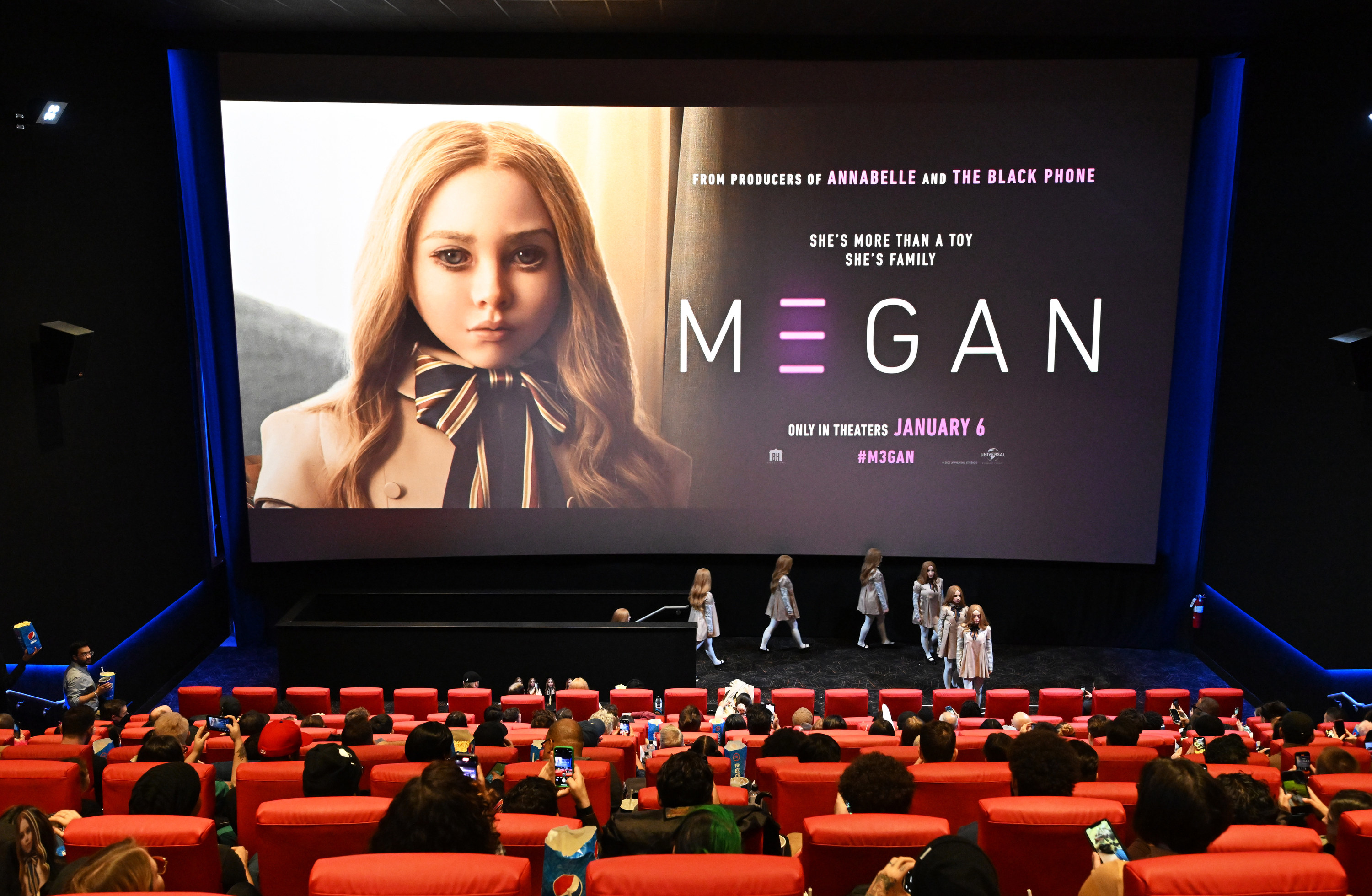 A photo of a press junket for M3GAN, with a large poster of the film showing the doll&#x27;s eerie face on stage