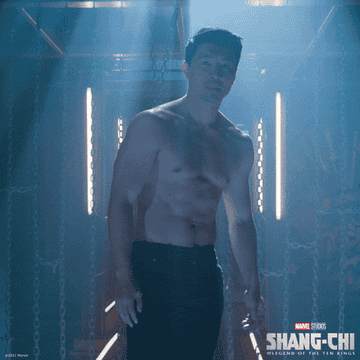 shang-chi is shirtless and stands in a room with rays of light coming from the ceiling