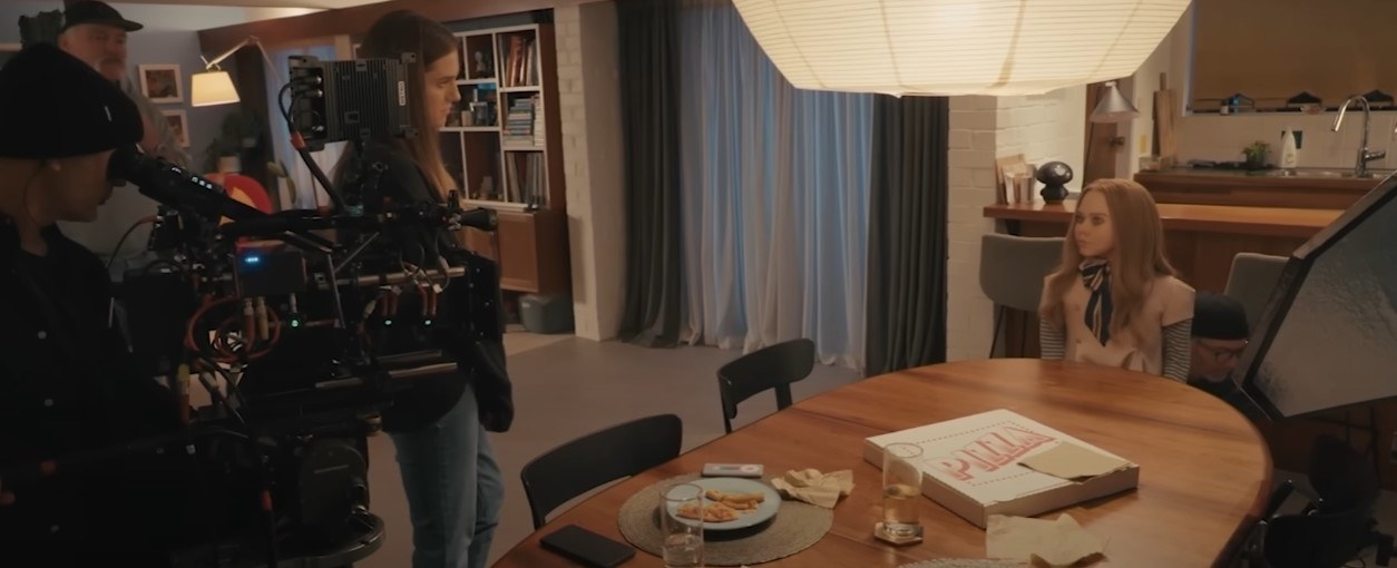BTS shot of Allison Williams with cameras behind her, looking at the M3GAN doll