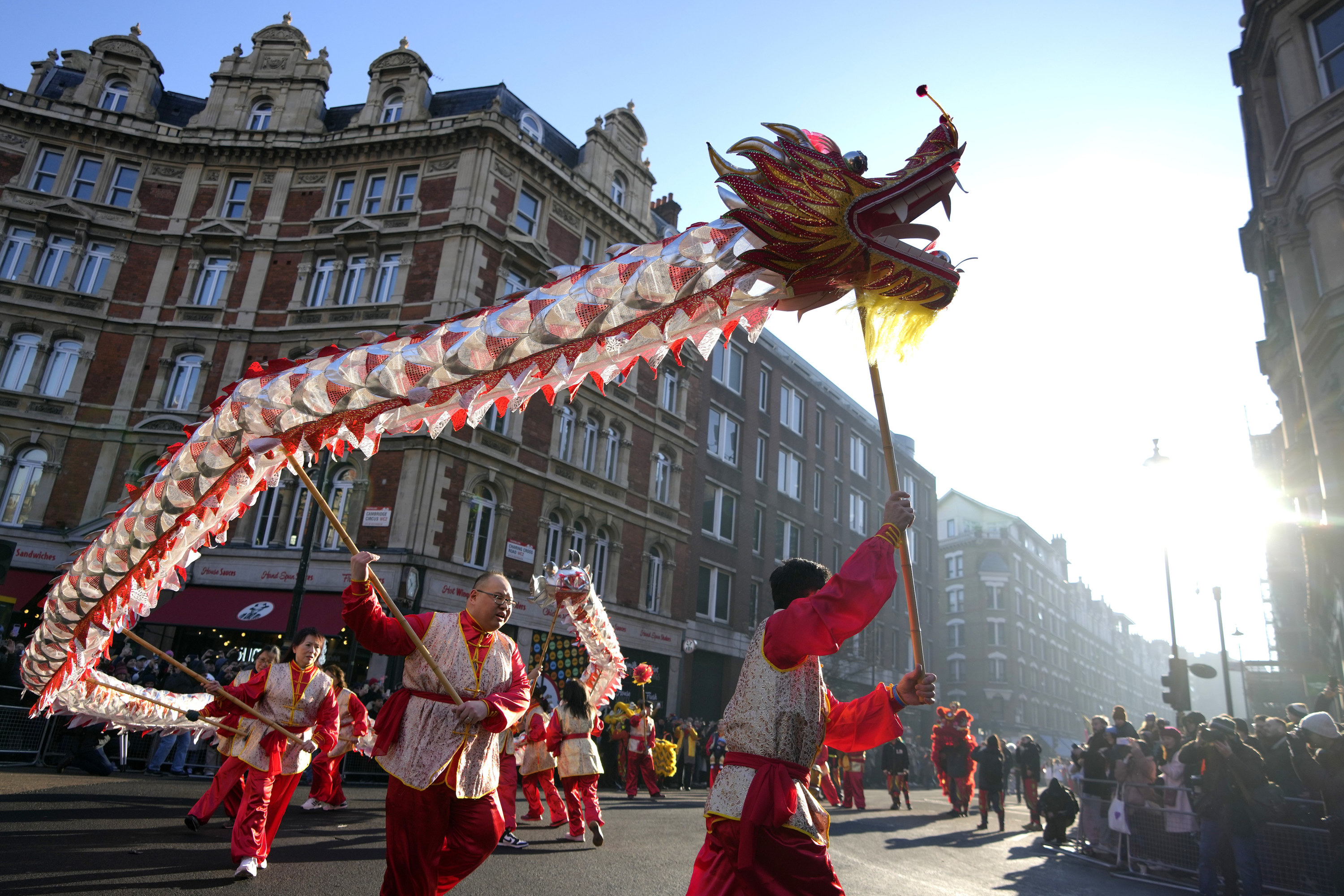 People dressed in red run through a street in London holding up a long paper dragon