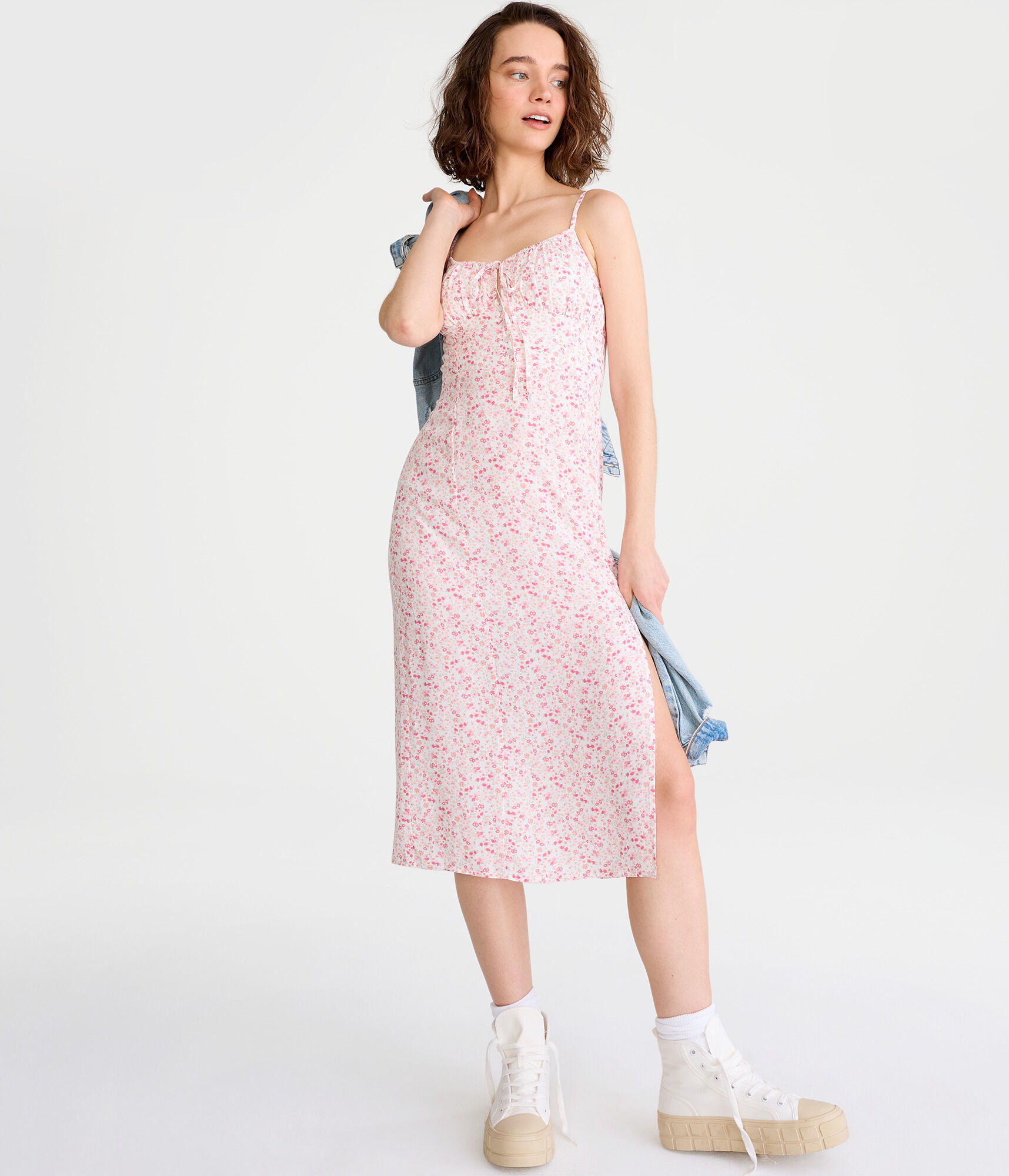 model in white midi spaghetti strap dress with small pink floral print, one slit, and a ruched bust
