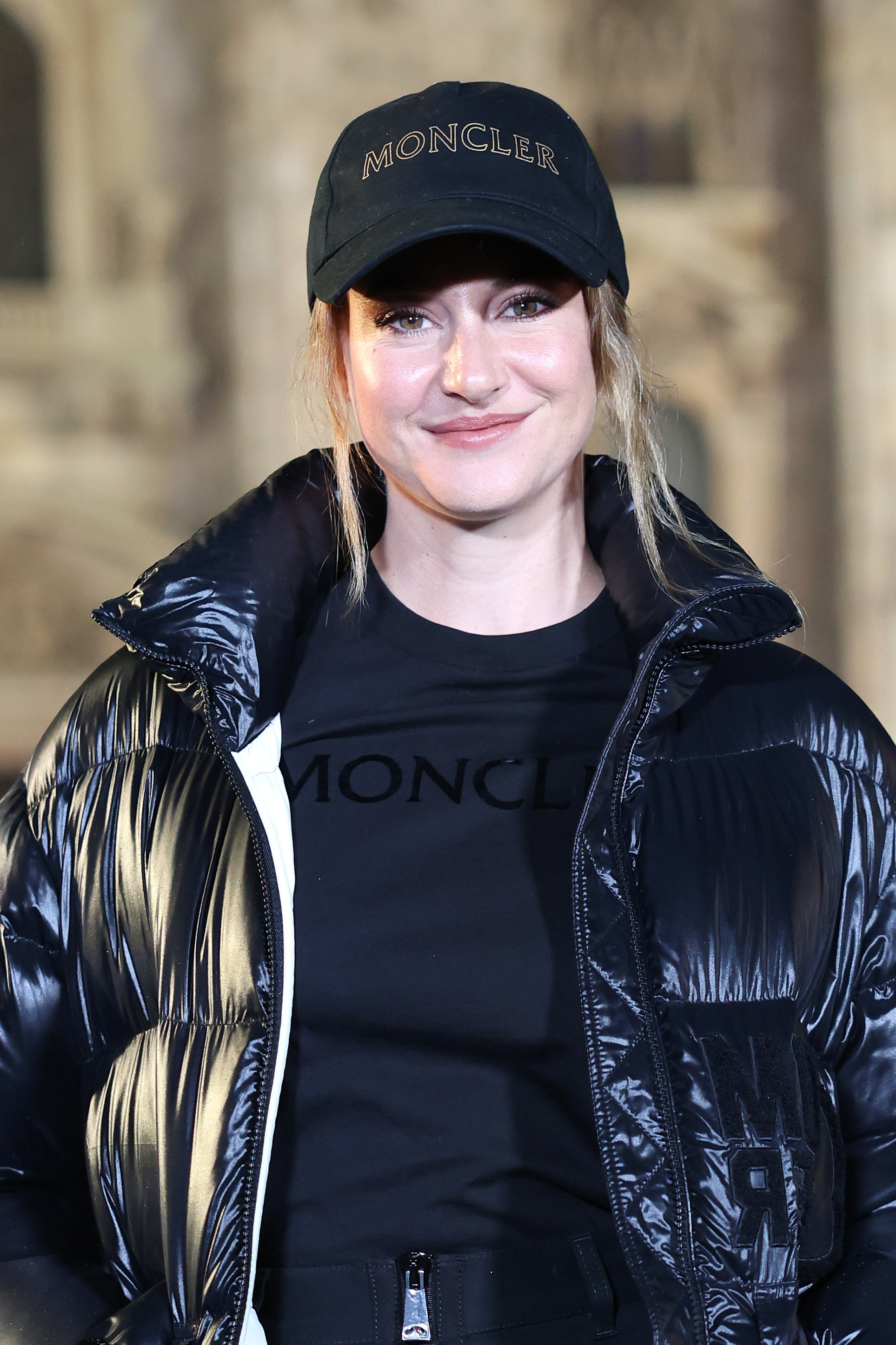 Shailene smiles as she wearing a a baseball cap and t-shirt which are both embossed with the brand name Moncler. She&#x27;s also wearing a puffer jacket