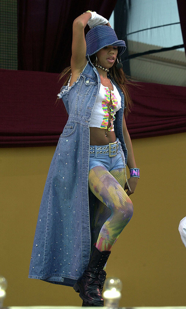 Kiely performing onstage in a crop tank top, leggings underneath denim shorts, a long bedazzled denim vest coat, and combat boots