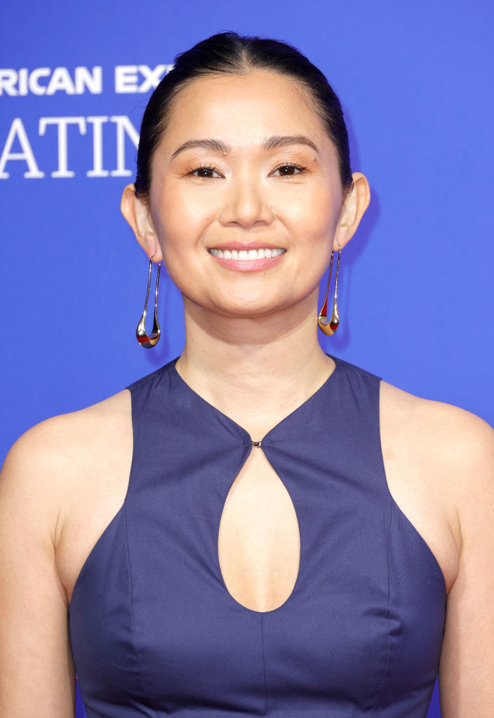 A closeup of Chau smiling as she rocks a halter outfit with a keyhole cutout on the chest. Her hair is pulled back in an updo that shows off drop earrings