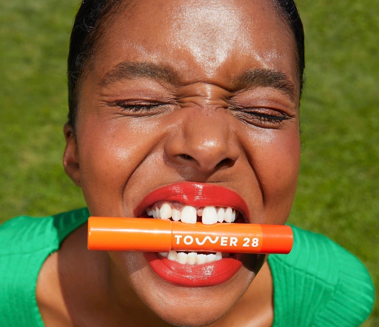 a person holding a tube of tower 28 lip balm between their teeth