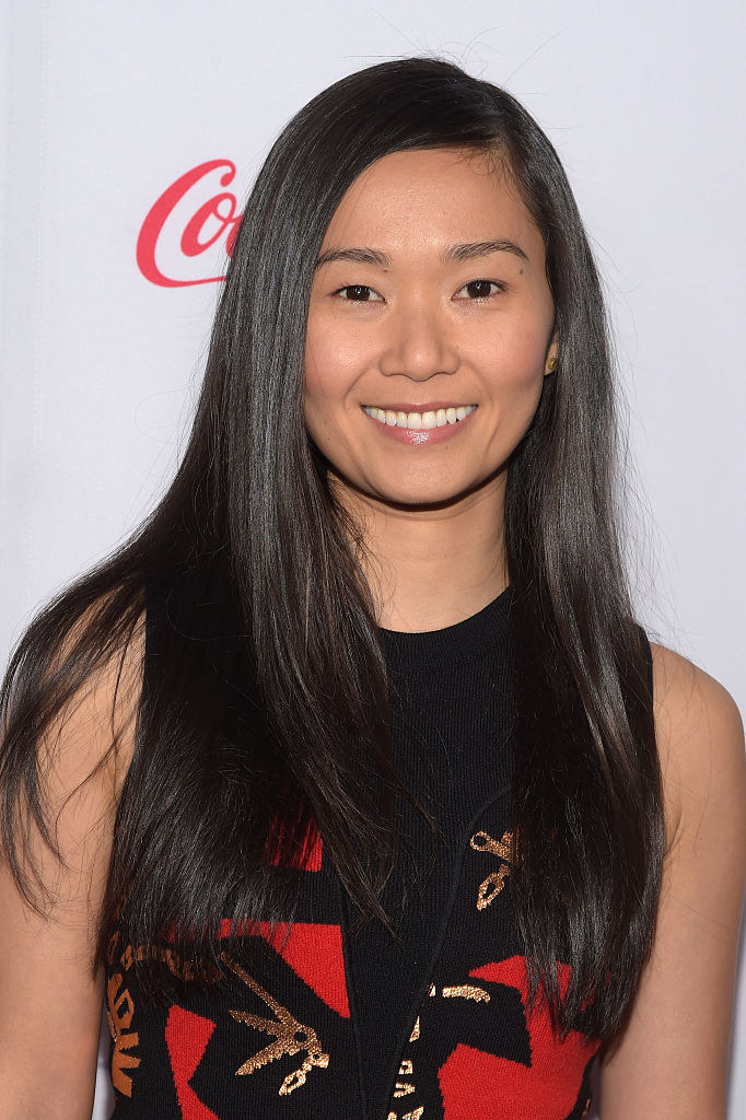 Chau smiles at a red carpet event while wearing a sleeveless outfit. Her hair is parted on one side and falls below her shoulders