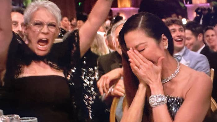 Jamie Lee Curtis with her arms raised in the air cheering as Michelle Yeoh puts her head in her hands when she won her Golden Globe award