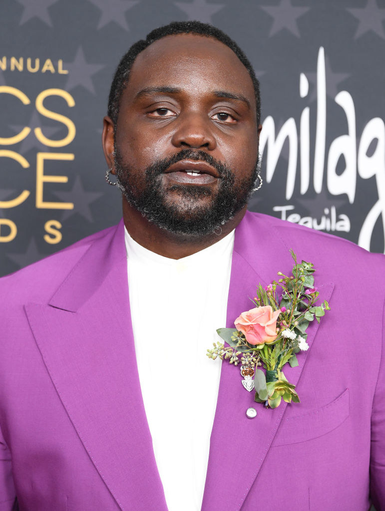 A closeup of Bryan at a red carpet event in a shirt and blazer adorned with a rose
