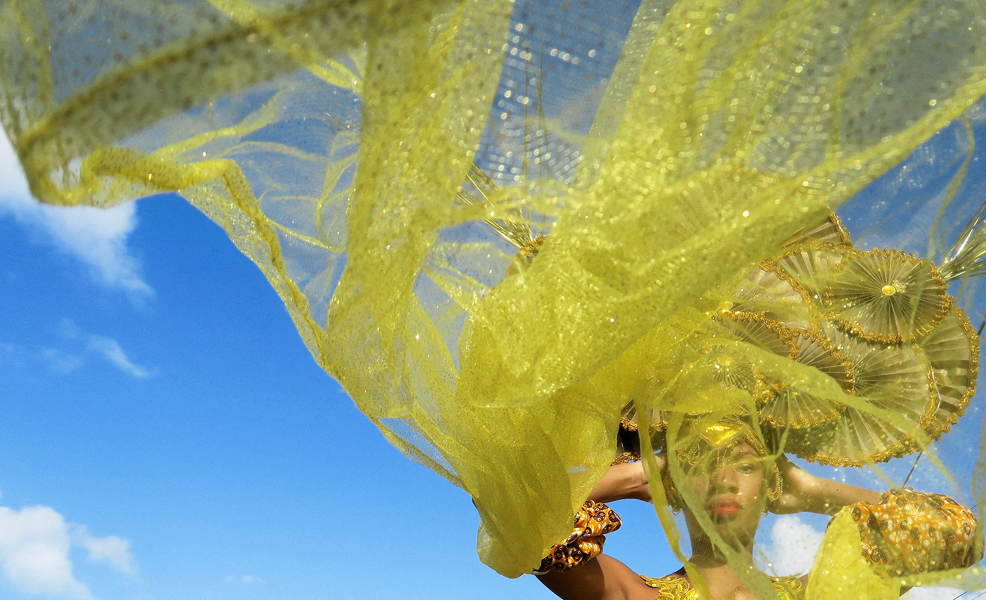 a shot of someone standing with their hands on their head and a huge yellow flowing veil blows in the wind