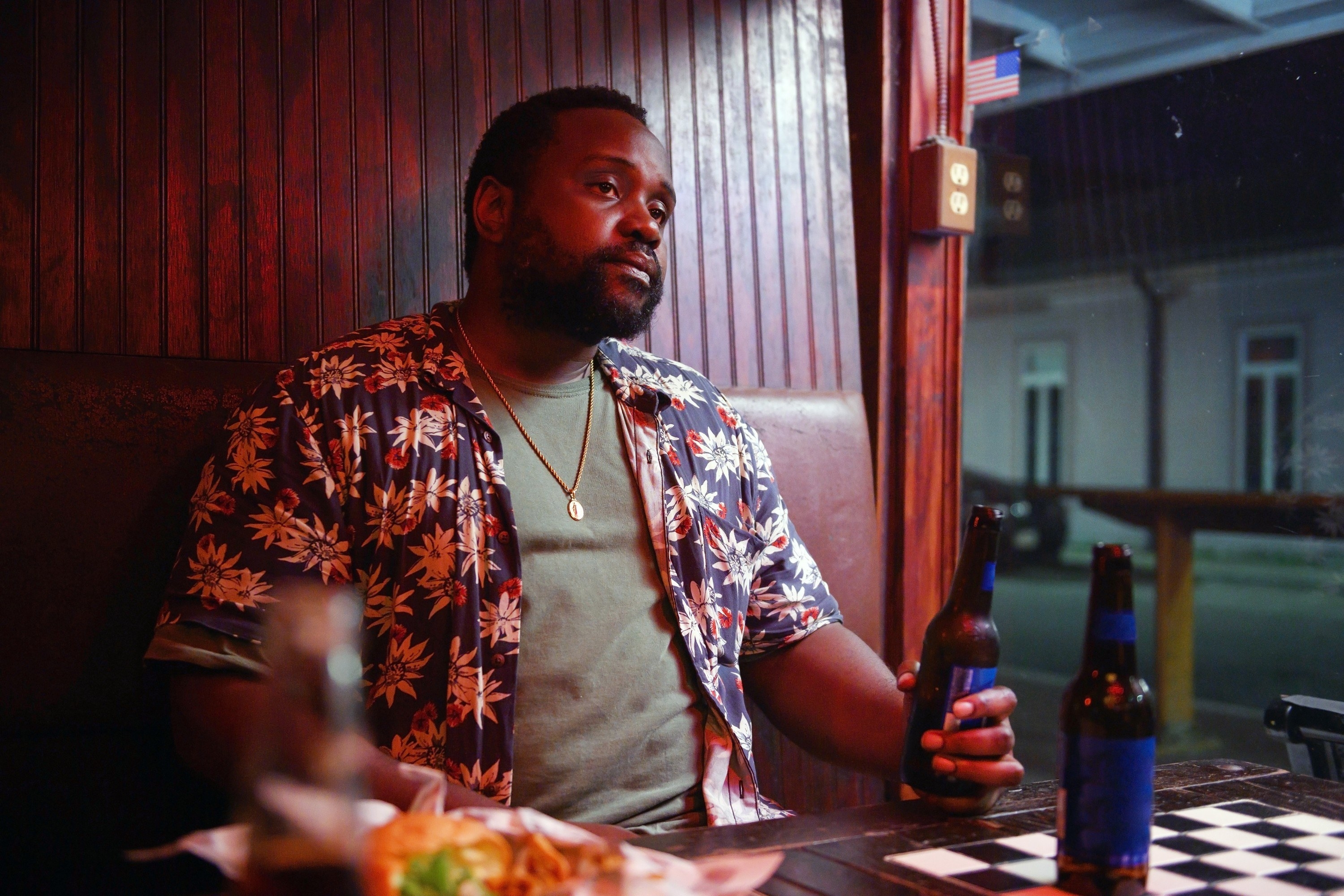 Henry sitting in a restaurant booth holding a bottle of beer in a scene in &quot;Causeway&quot;