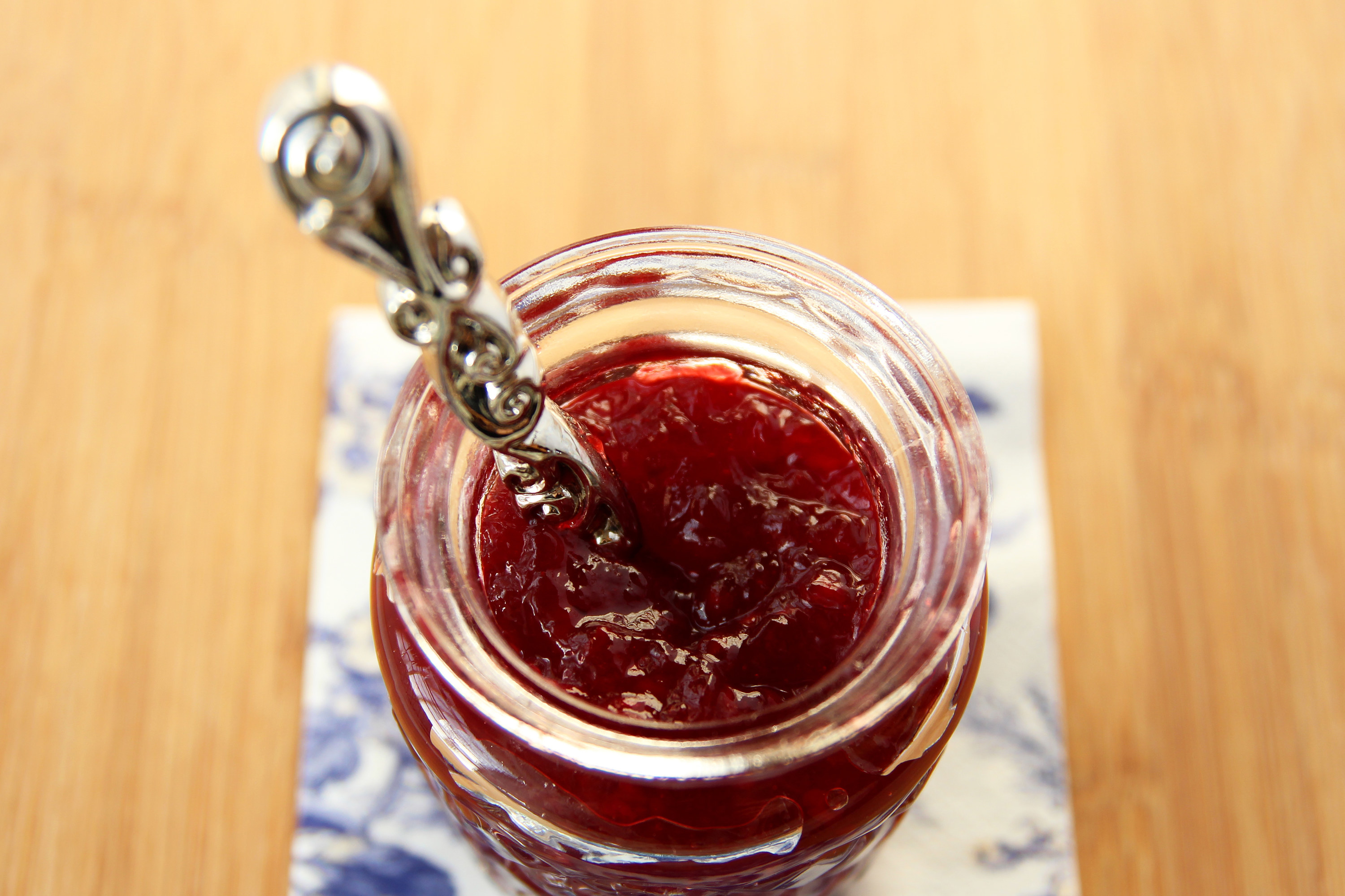 An overhead shot of an open jar of jam with a spoon inside of it
