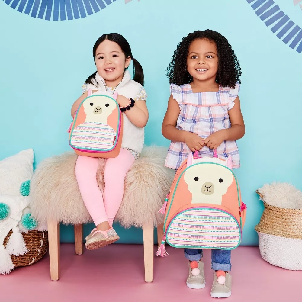 Child models holding pastel colored back pack shaped like a llama