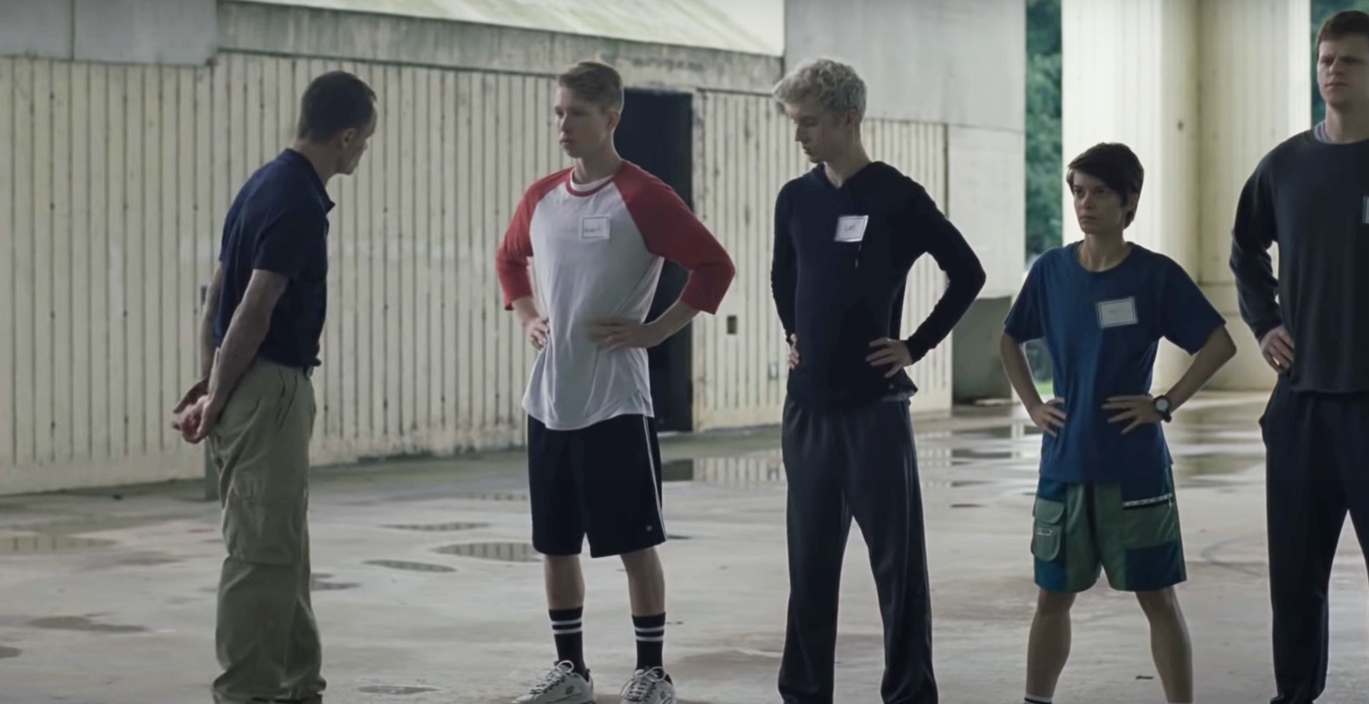 teens and young boy standing in a line while a boot camp couch yells at them