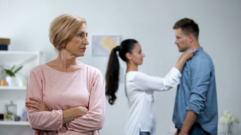 woman with arms crossed while a couple stand affectionately behind