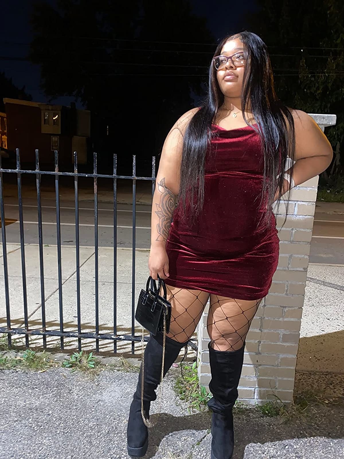 Reviewer wearing red velvet mini dress with fishnets and black knee high boots