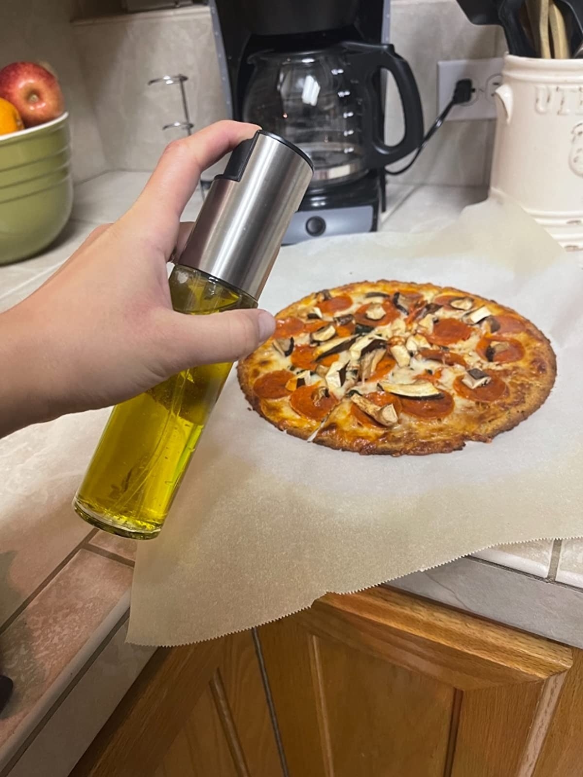 hand holding oil mister above veggie and pepperoni pizza