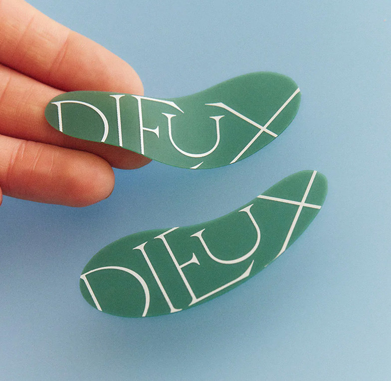 Green under-eye masks with Dieux&#x27;s logo covering them in a thin, serif font