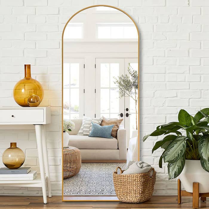 an arched mirror with a shiny metallic frame leaning against a painted brick wall