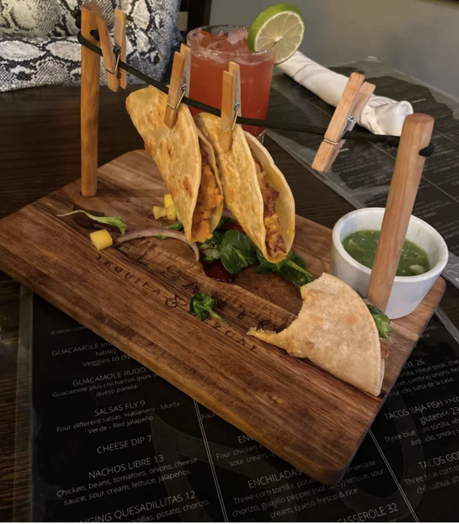 Tacos above a wooden cutting board and hanging from what look like clothespins