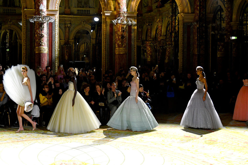 model with a dress attached to the side leading other models with gowns worn normally