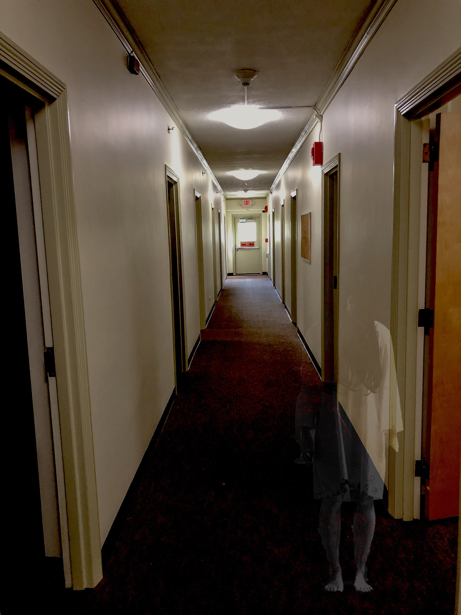 empty hallway with a ghost-like person standing creepily in the corner