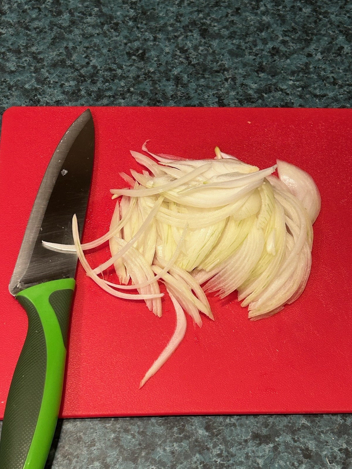 A cutting board with sliced onions next to a knife