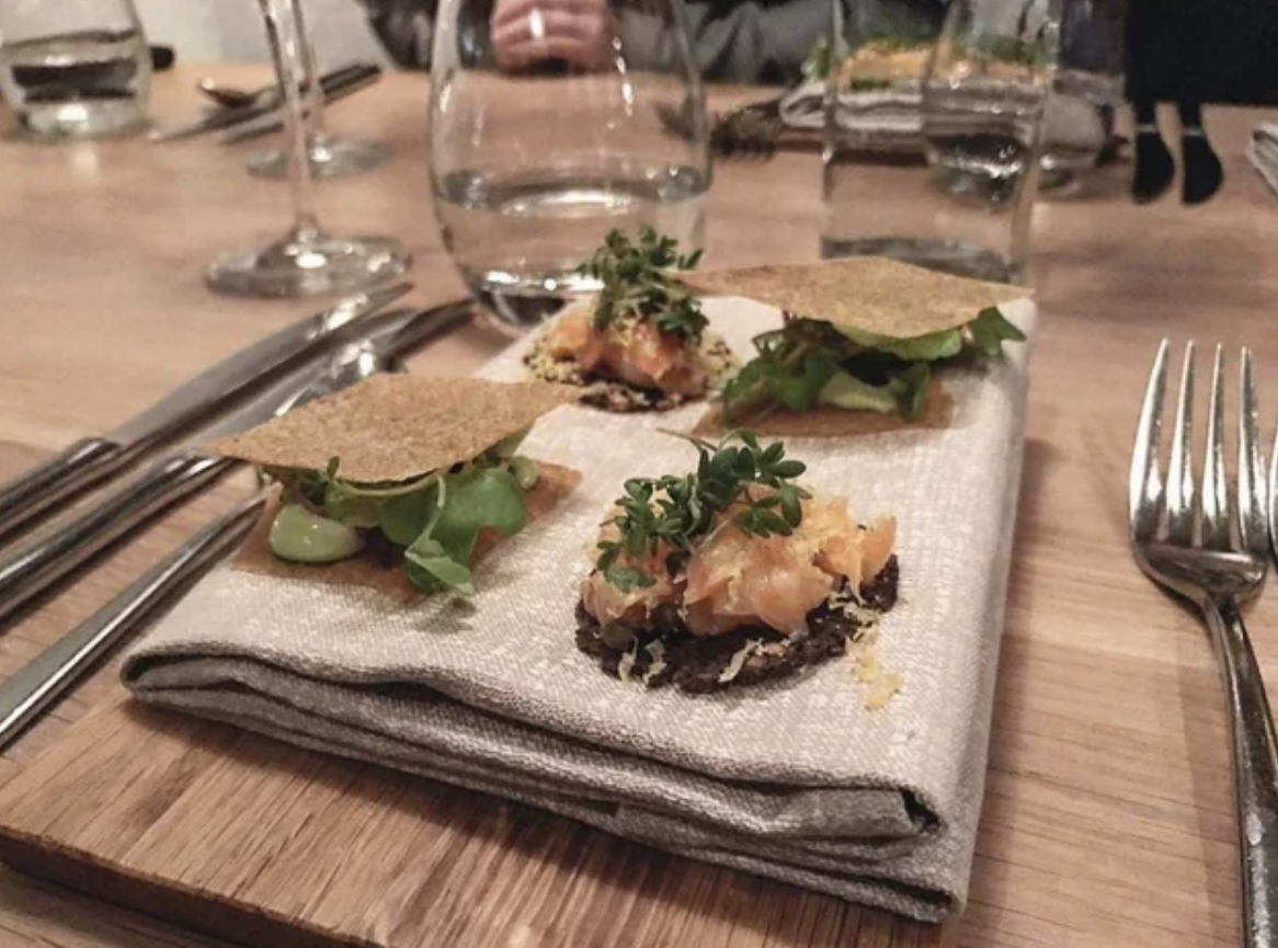 Hors d&#x27;oeuvres of some kind with crackers and garnish, served on a folded napkin on top of a wood cutting board
