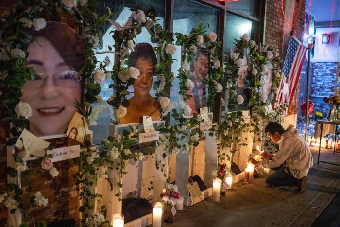 A man kneels and lights a candle beside a wall showing pictures of older Asian Americans surrounded by flowers