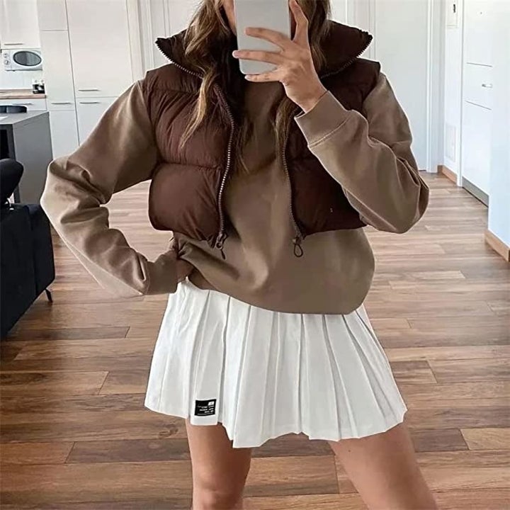 A person wearing the vest with a hoodie and skirt