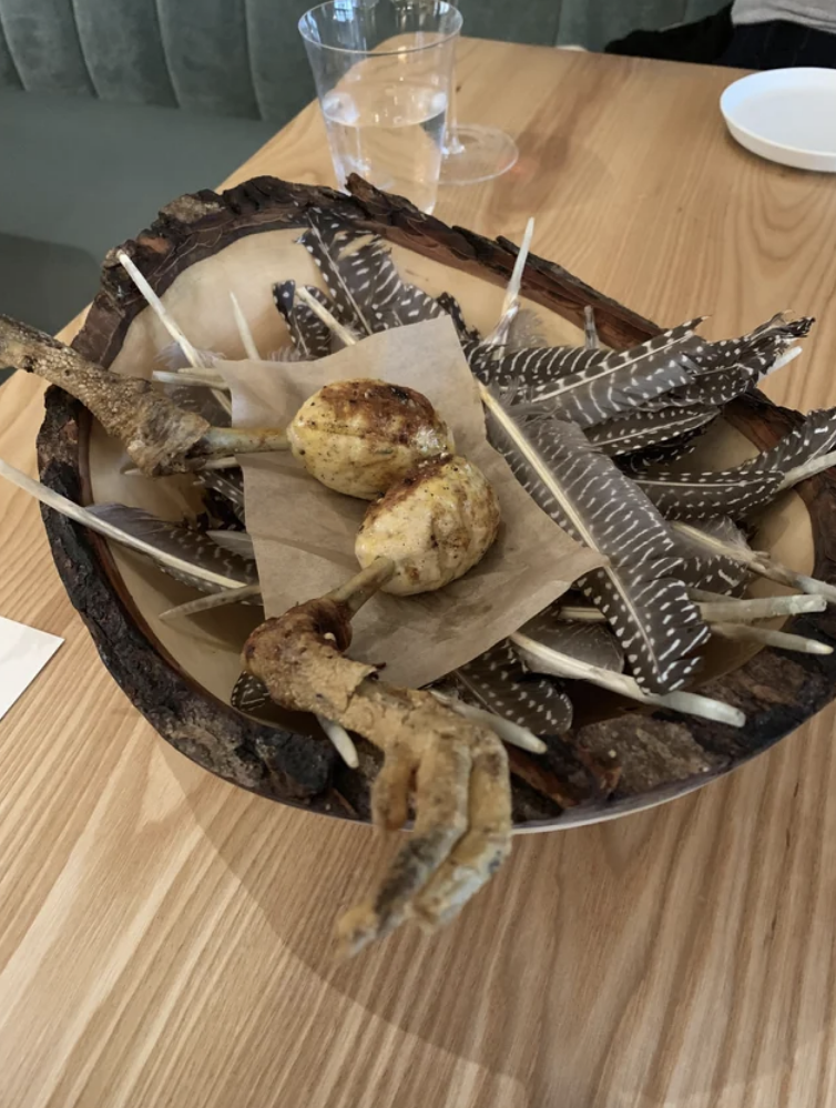 Some kind of drumsticks on a plate that looks a bit like a nest, with bird feathers, sticks, and bird feet