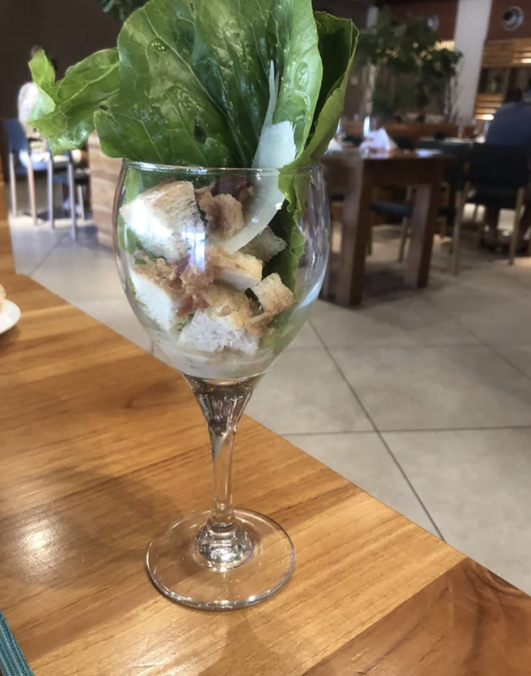 Large, whole lettuce leaves, onions, and croutons in a wine glass