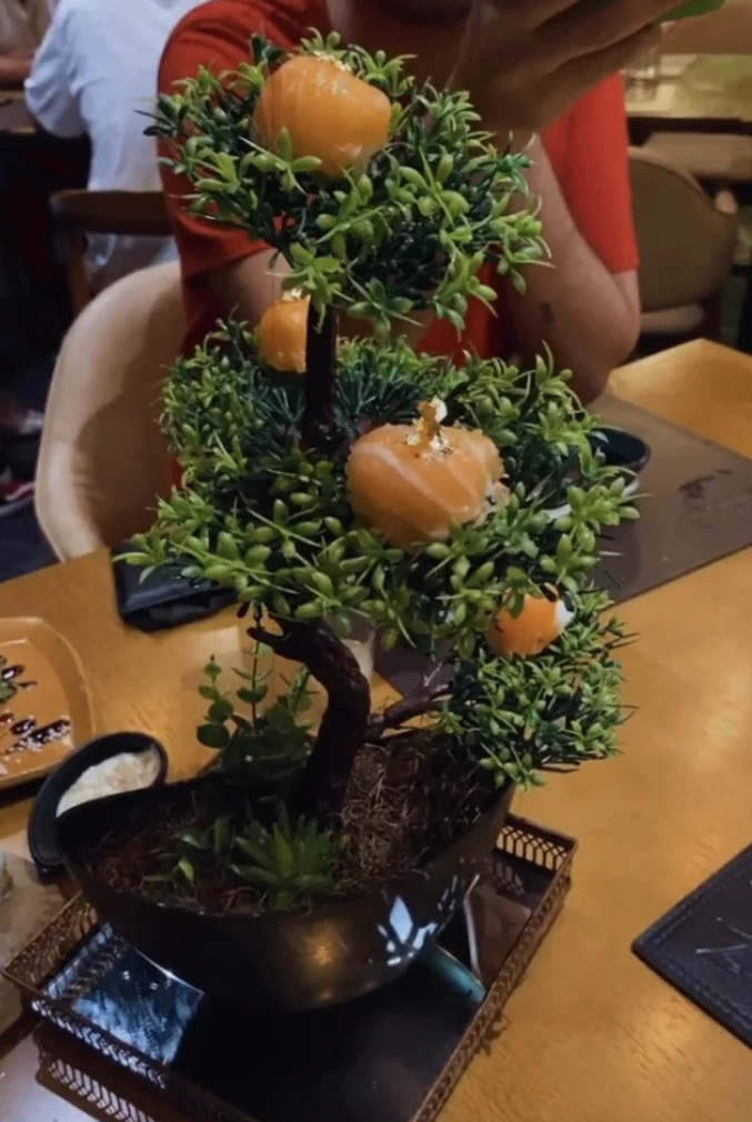 A bonsai-type tree on a restaurant table with sushi stuck in it