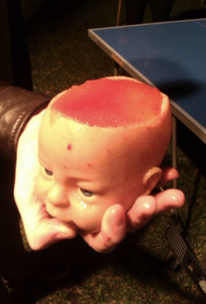 A drink in a mug in the shape of a baby doll&#x27;s head with the top of the head missing