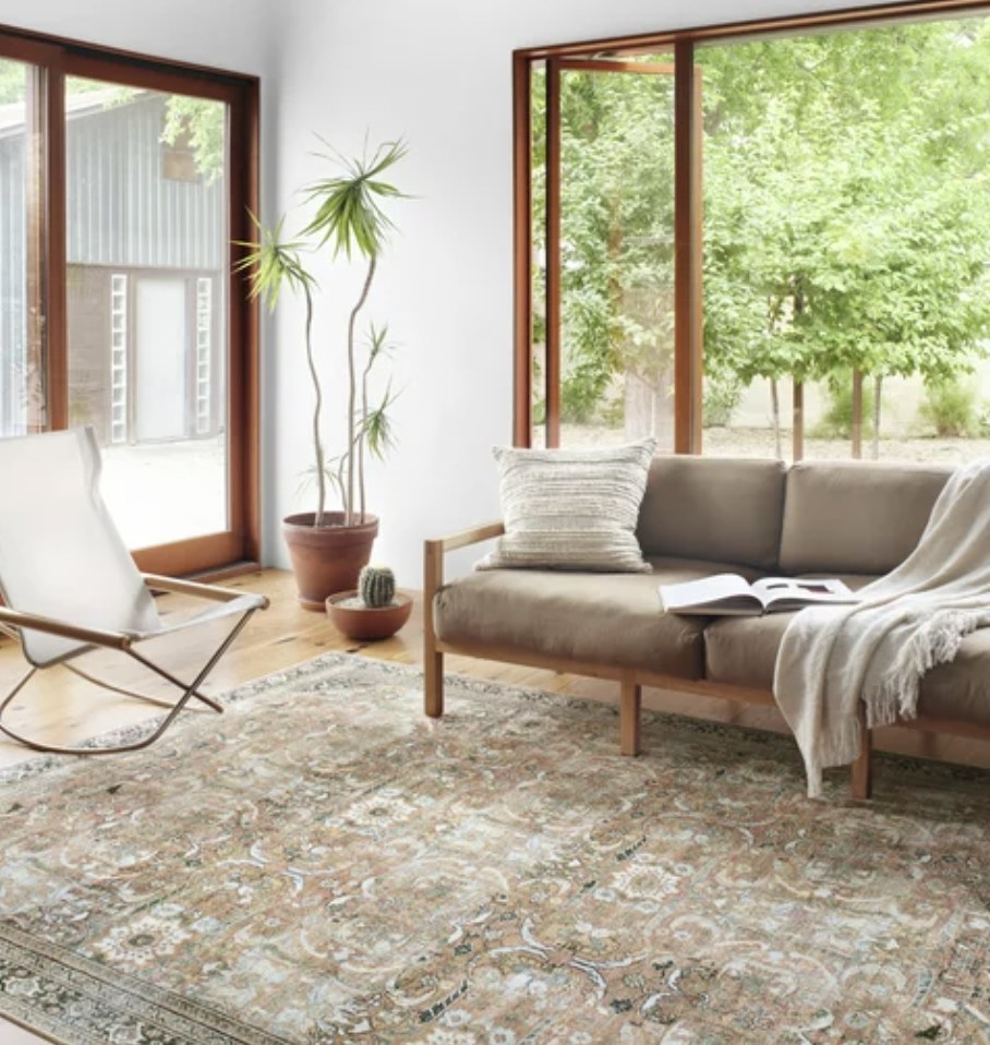 A beige Oriental rug in a living room with a tan couch and white rocking chair