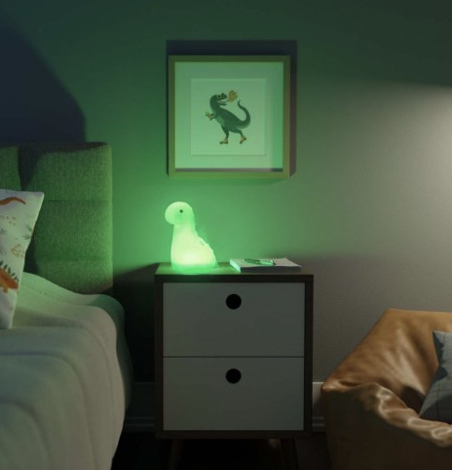 A dinosaur-shaped night-light glowing green on a bedside table