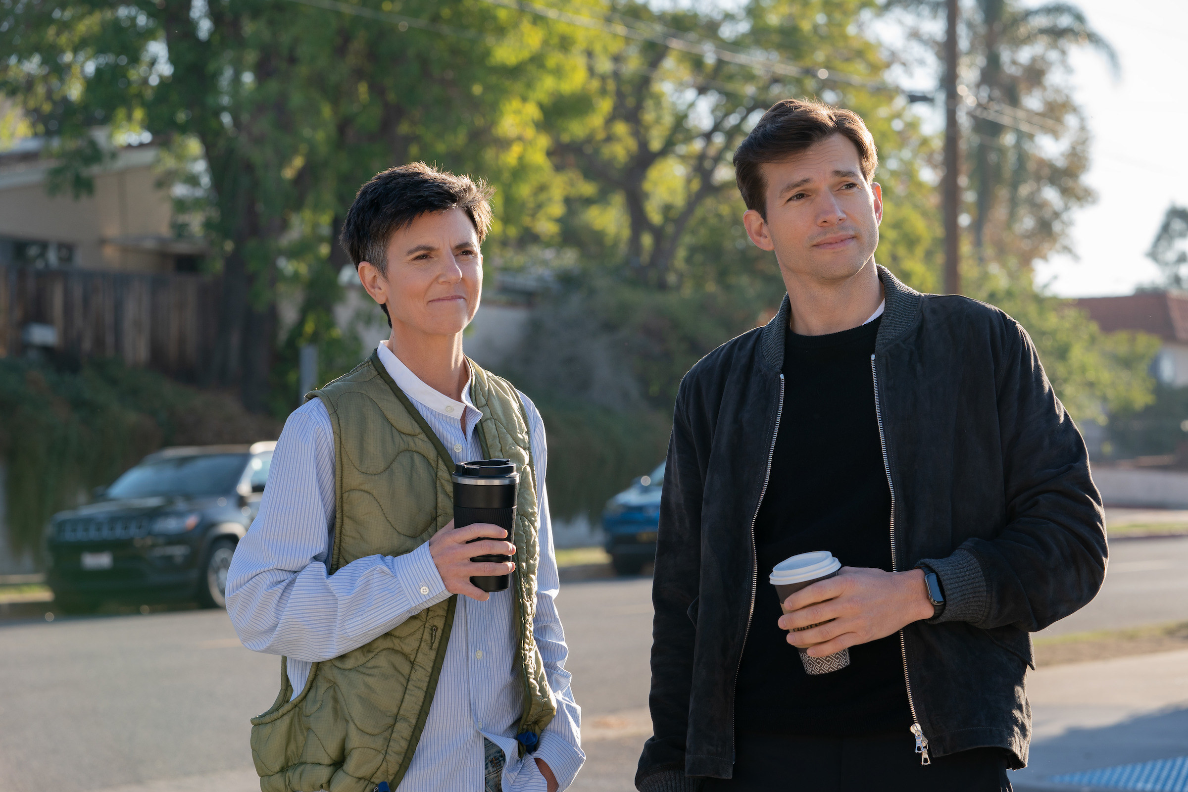 Tig Notaro and Ashton standing outside and holding coffee in a scene from the film