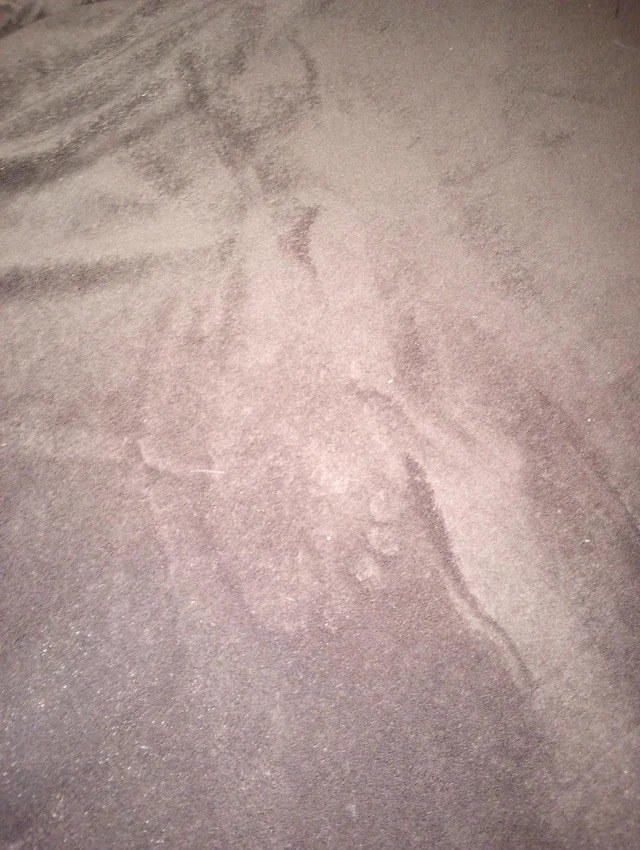 A blanket on a bed with the light outline of a foot