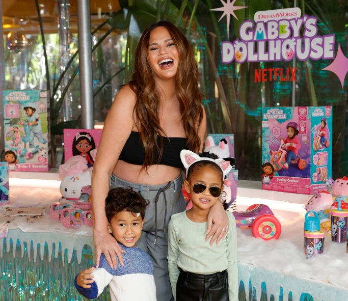 Chrissy laughing as she holds her two eldest children at a Netflix event for Gabby&#x27;s Dollhouse