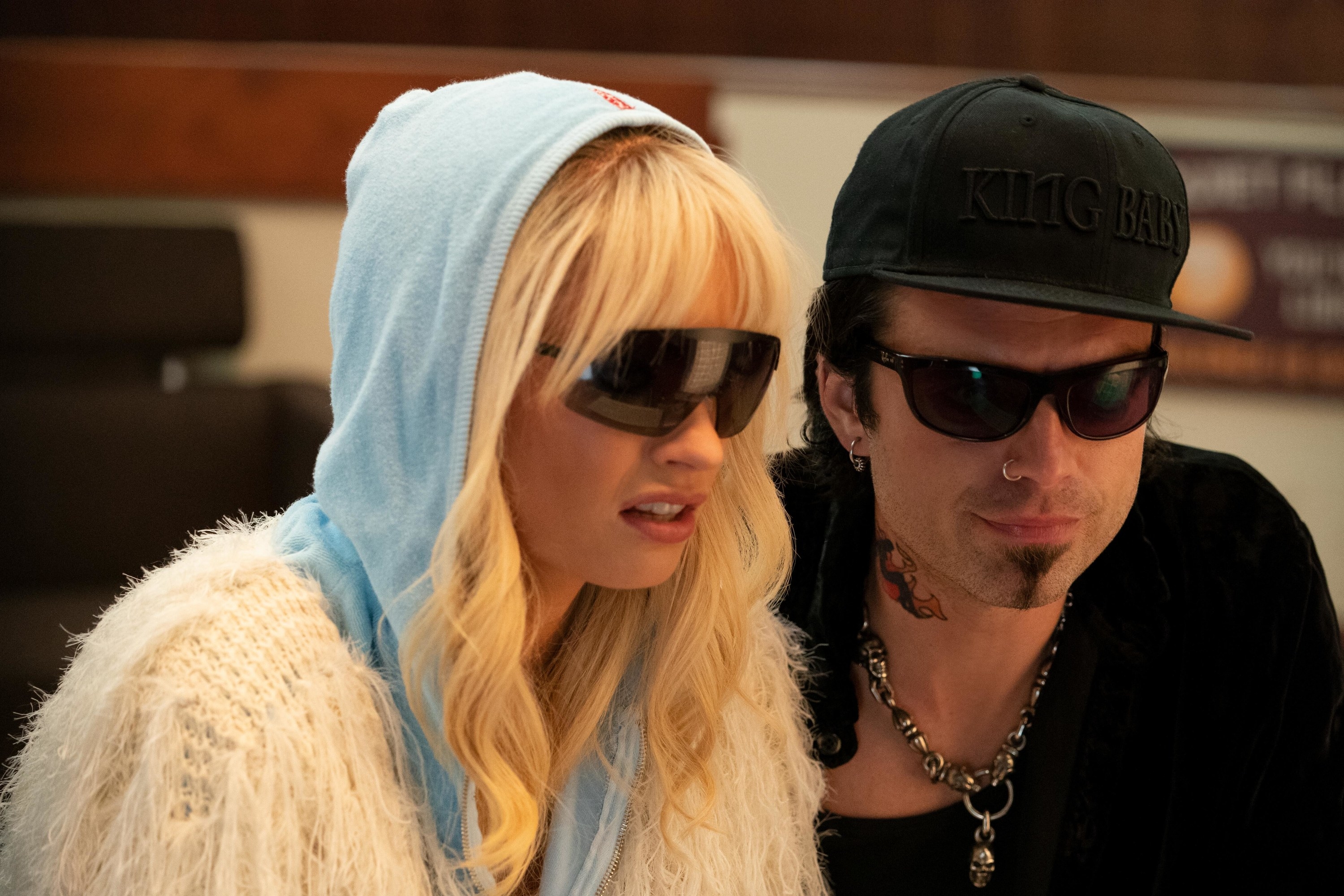 Pam and Tommy, both wearing sunglasses, as they crouch down to look at something in a scene from the series