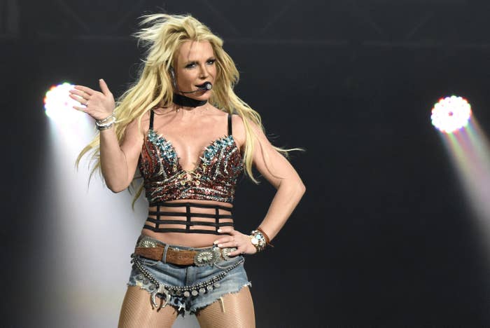 Britney performing onstage with her hand on her hip as she rocks a sequined crop top and denim shorts