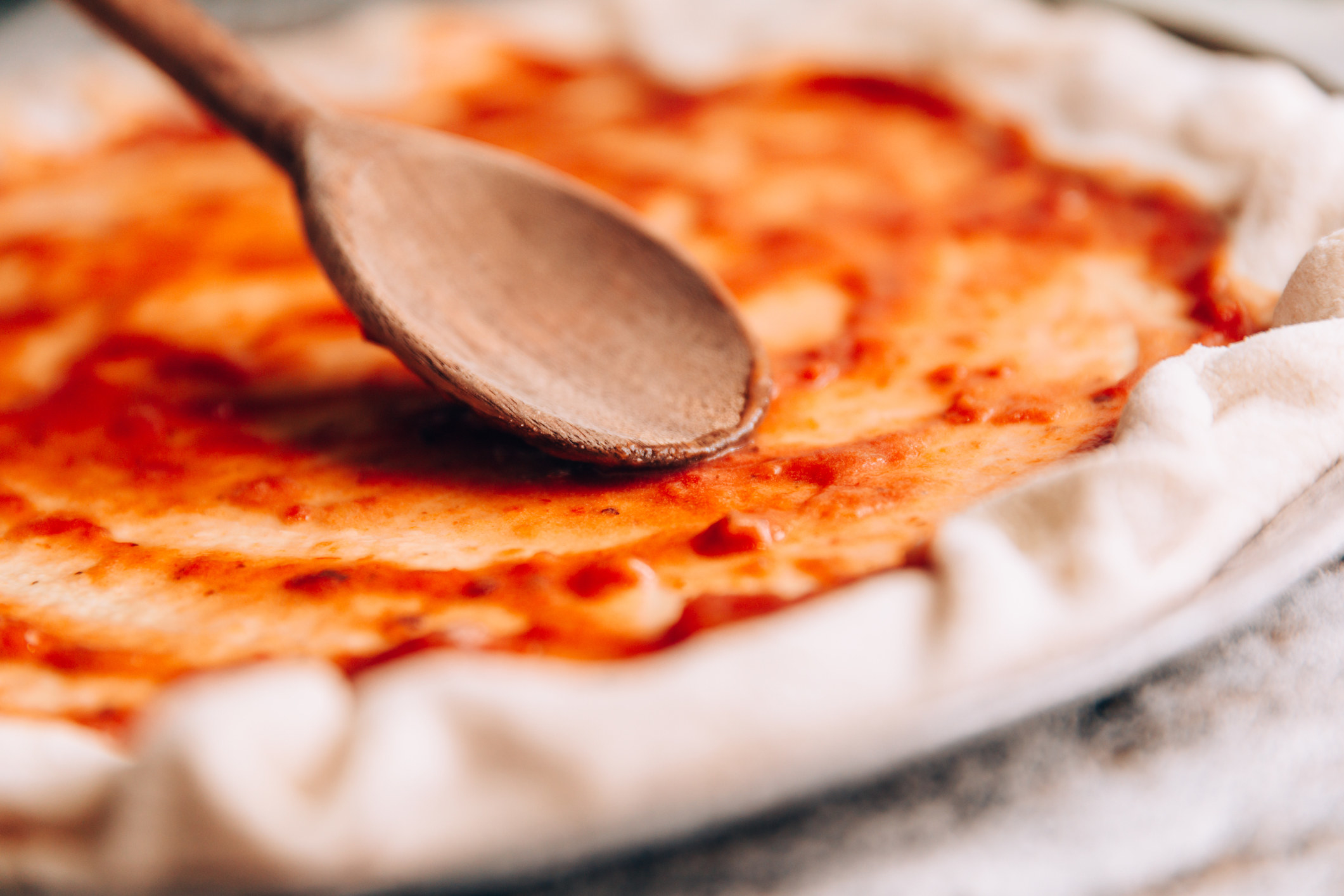 spoon spreading sauce over pizza dough