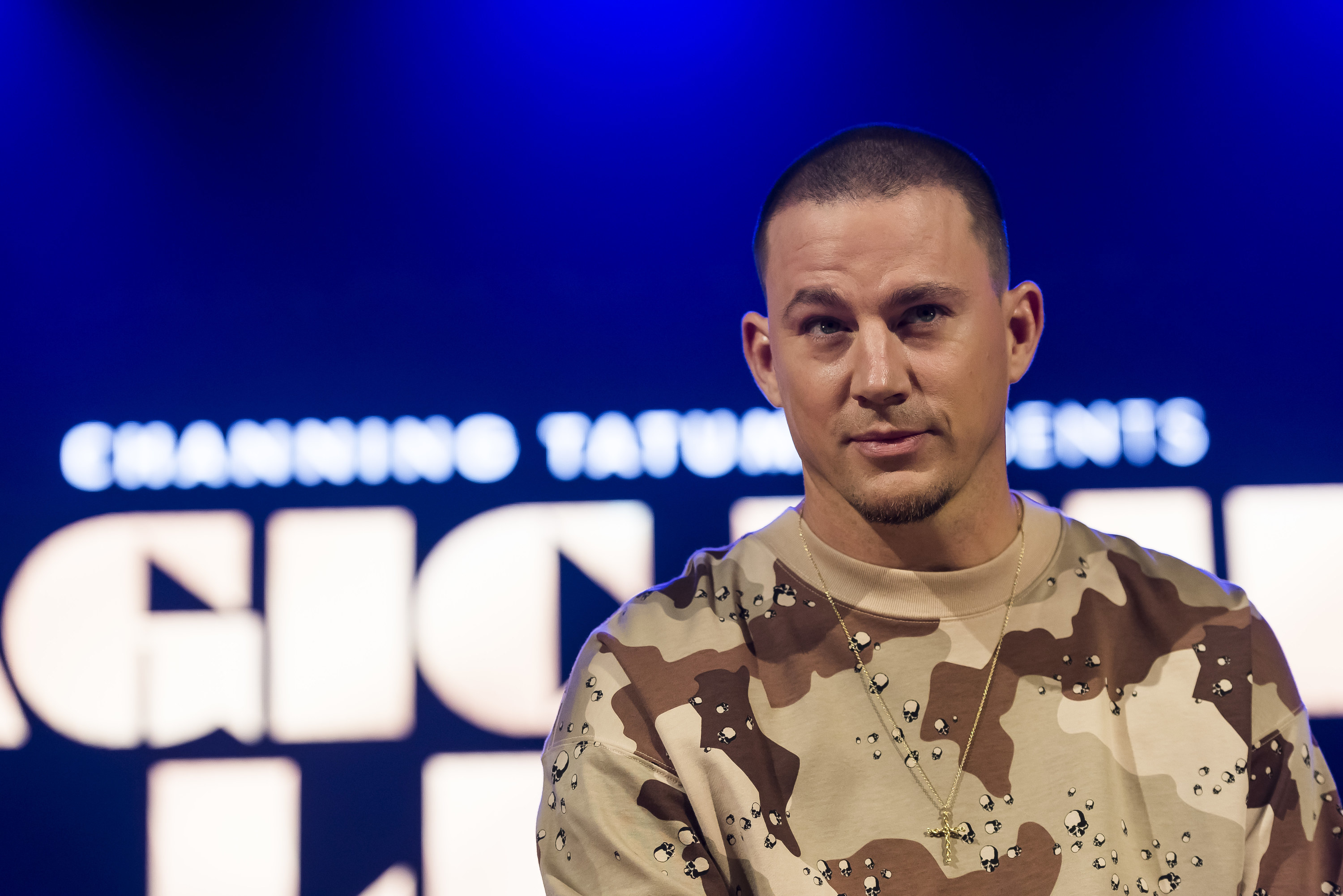 A closeup of Channing wearing a camouflage sweatshirt and a cross chain