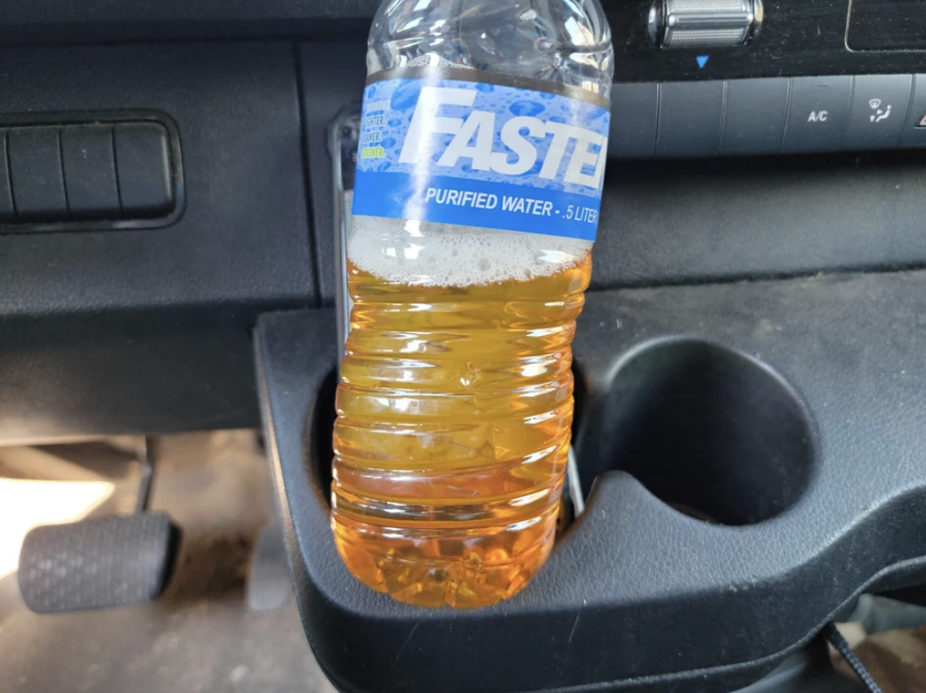 A plastic bottle with yellow liquid in it in the car&#x27;s cupholder