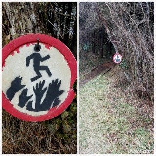 A warning street sign of a stick person jumping over hands at the entrance of a wooded area