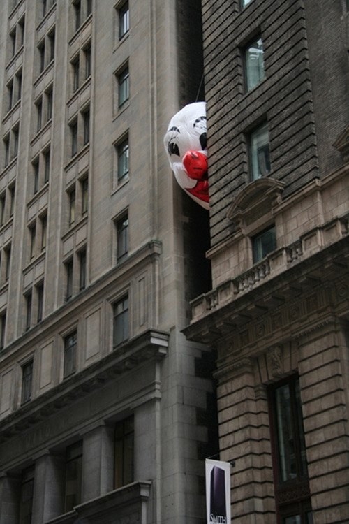 A large clown face balloon wedged between two high rise buildings