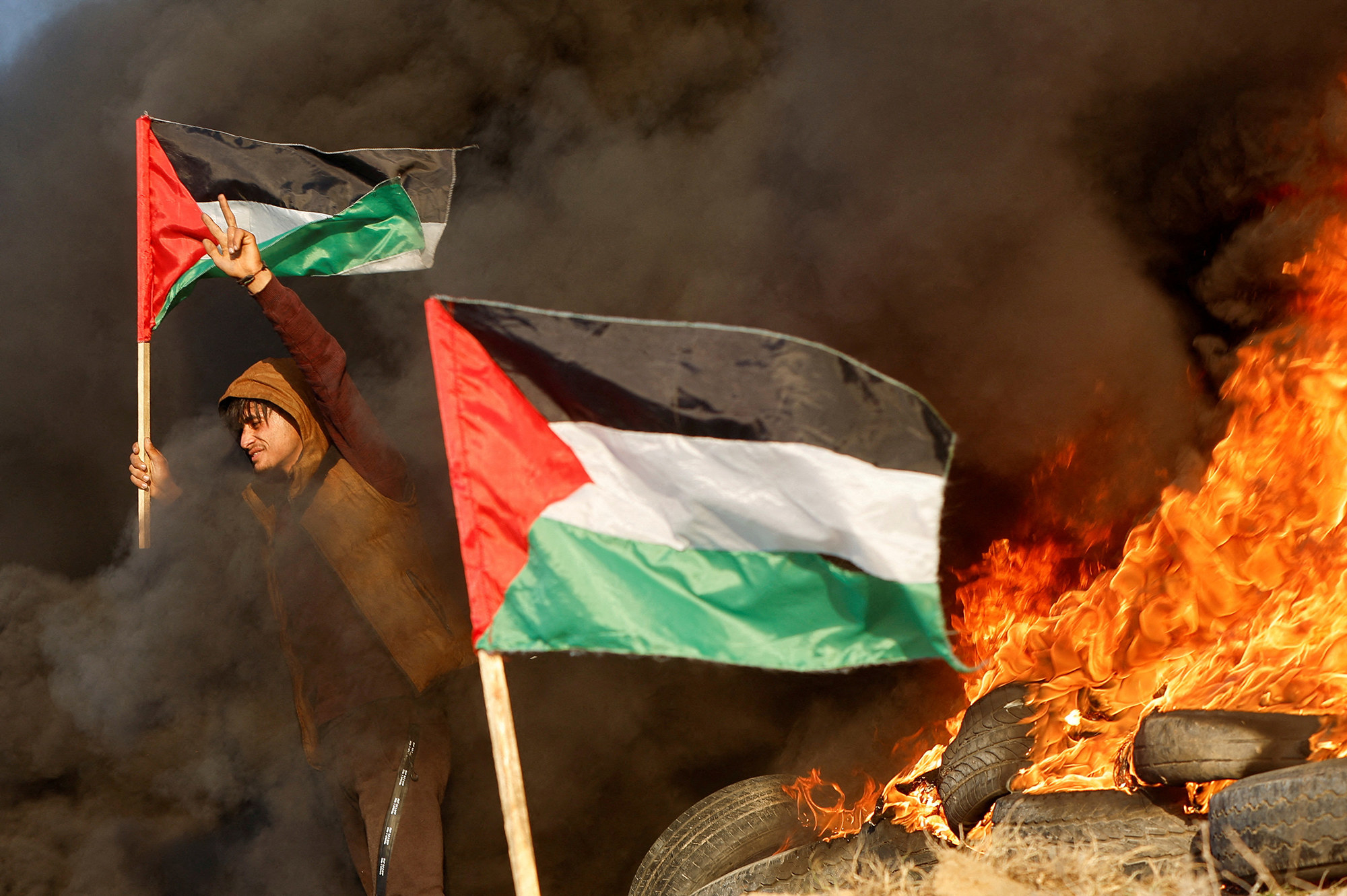 a man holding a palestinian flag surrounded by smoke and fire