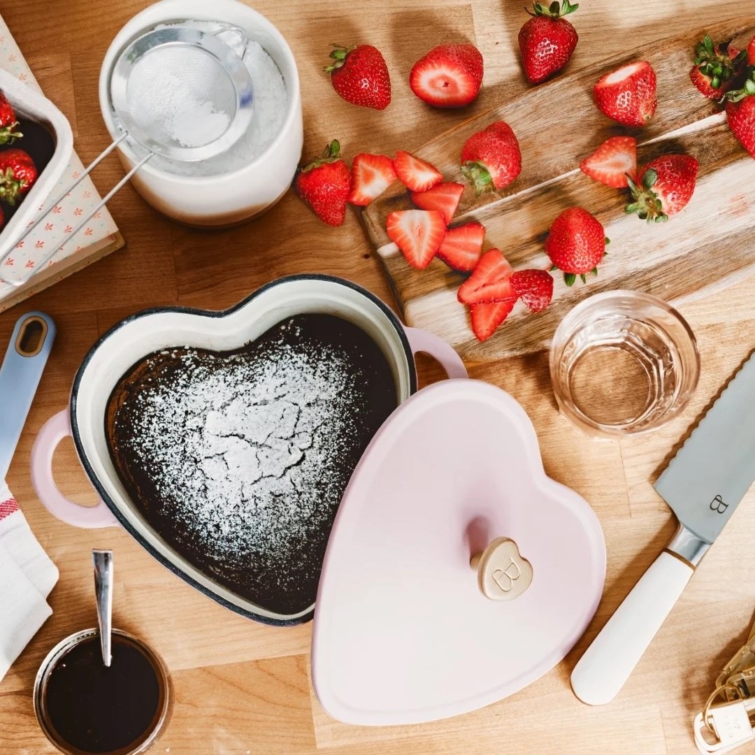 A pink heart-shaped pot with brownies in it and kitchen utensils around it