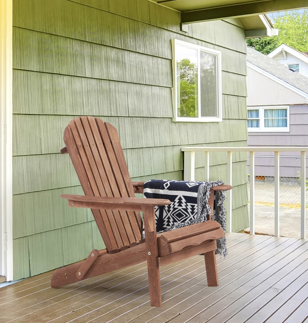 A wooden Adirondack chair on a porch with a blanket on it