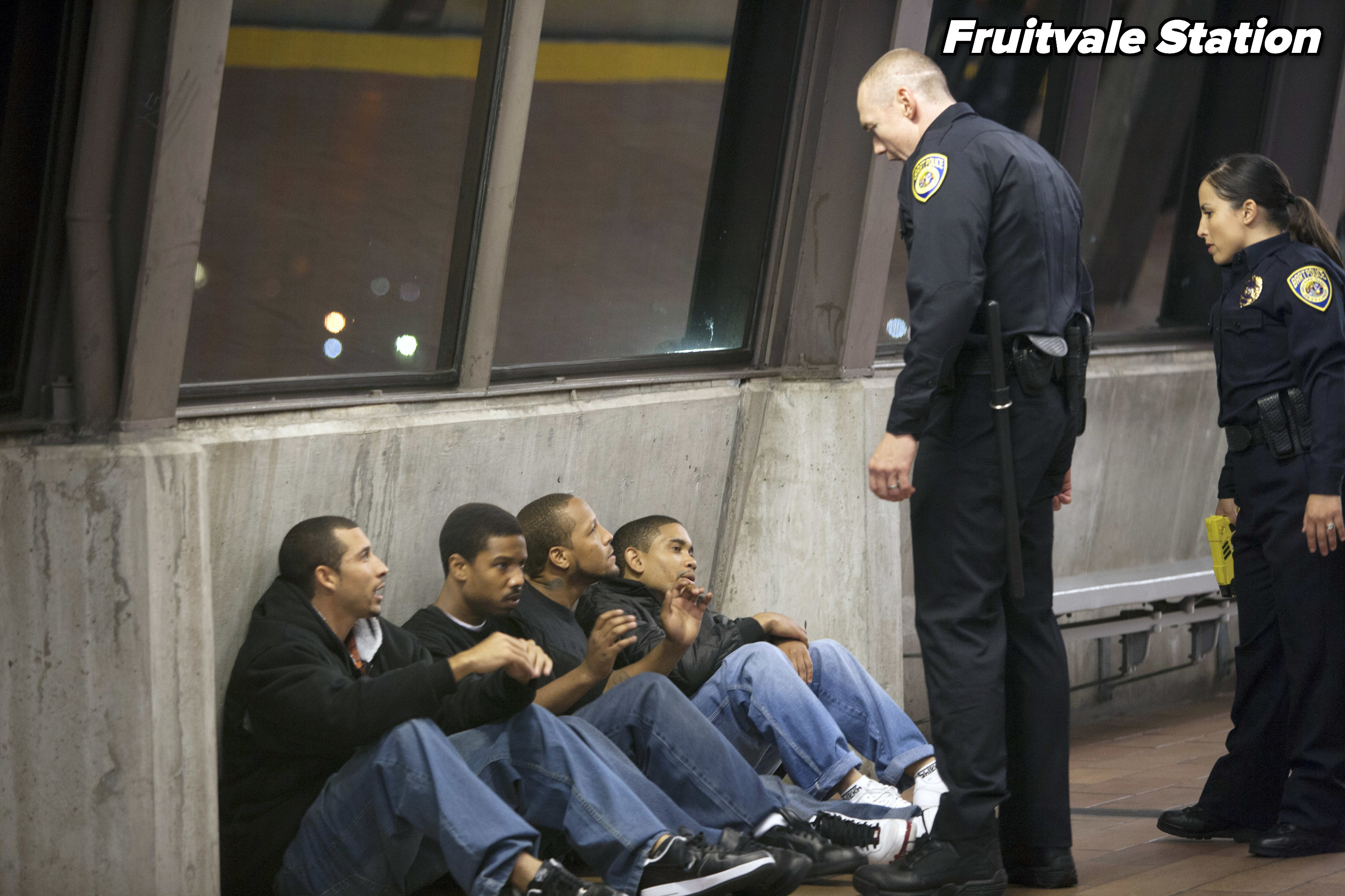 Two cops standing over four young men sitting on the ground from &quot;Fruitvale Station&quot;