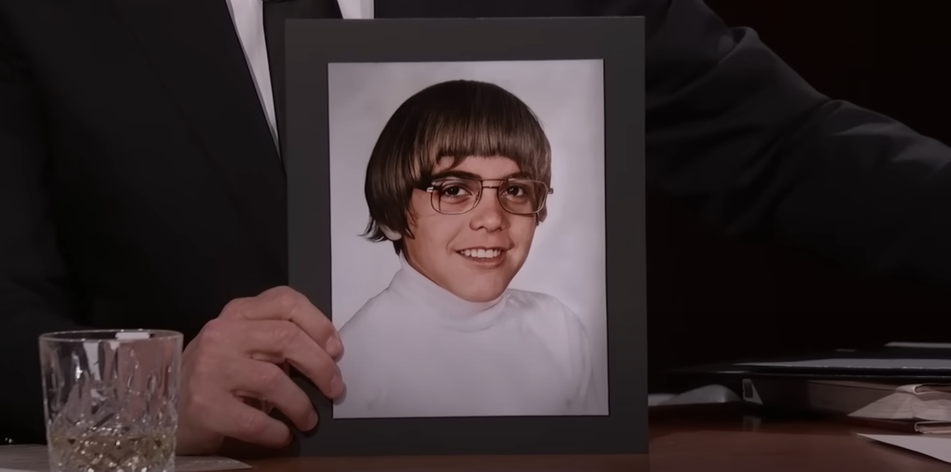 clooney wearing a turtleneck, glasses, and a bowl cut with shorter uneven bangs